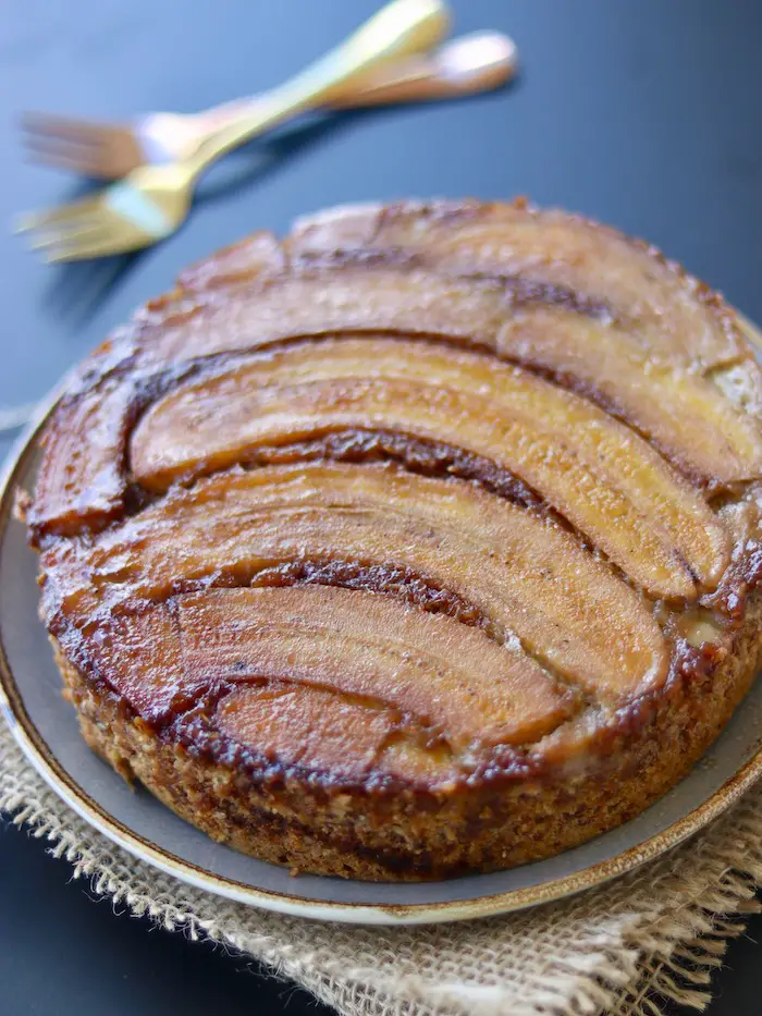 bolo vegano de banana caramelada servido em um prato com uma fatia cortada