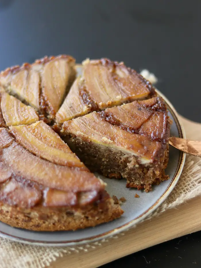 bolo vegano de banana caramelada servido em um prato com uma fatia cortada