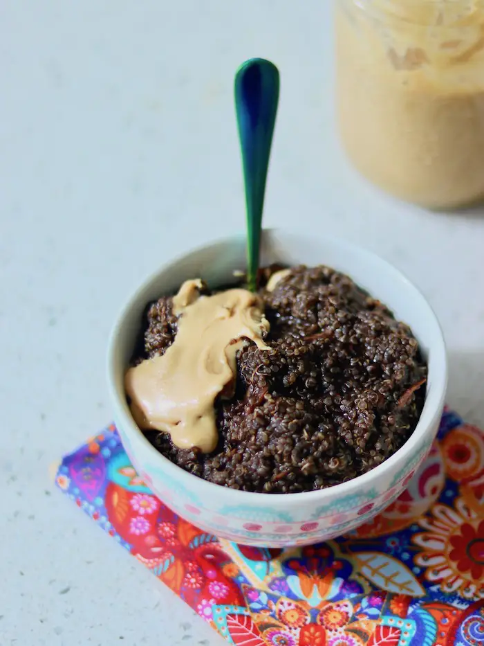 mingau de quinoa de chocolate e coco seco ralado servido em uma cumbuca com banana e pasta de amendoim caseira