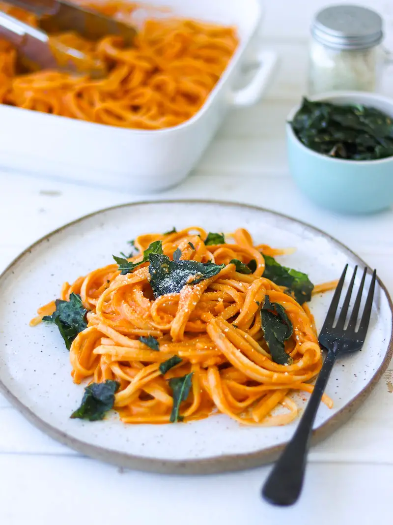 macarrão ao molho de pimentão vermelho assado servido com parmesão vegano e chips de couve