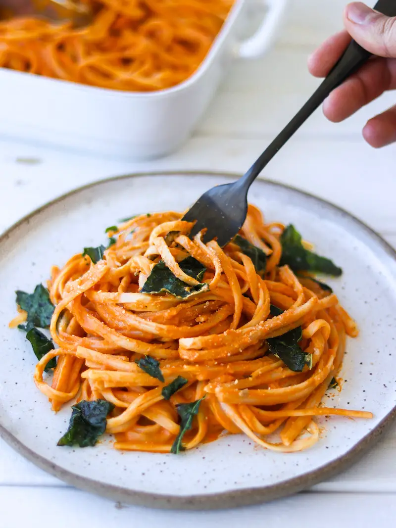 macarrão ao molho de pimentão vermelho assado servido com parmesão vegano e chips de couve