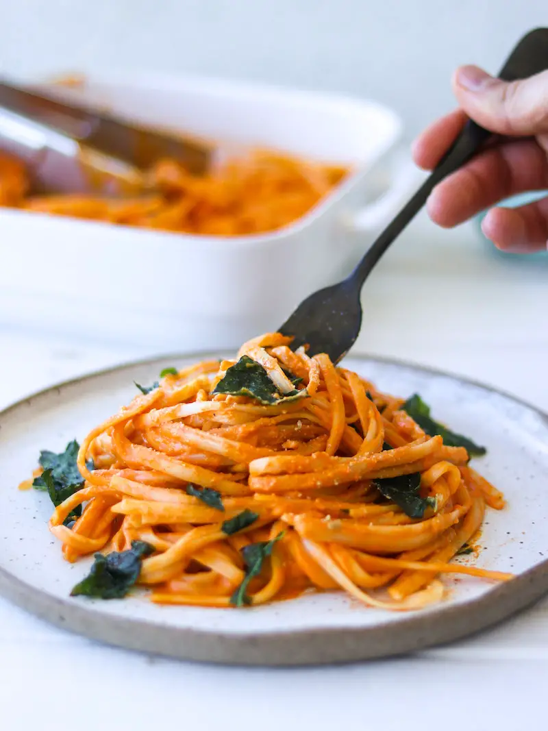 macarrão ao molho de pimentão vermelho assado servido com parmesão vegano e chips de couve