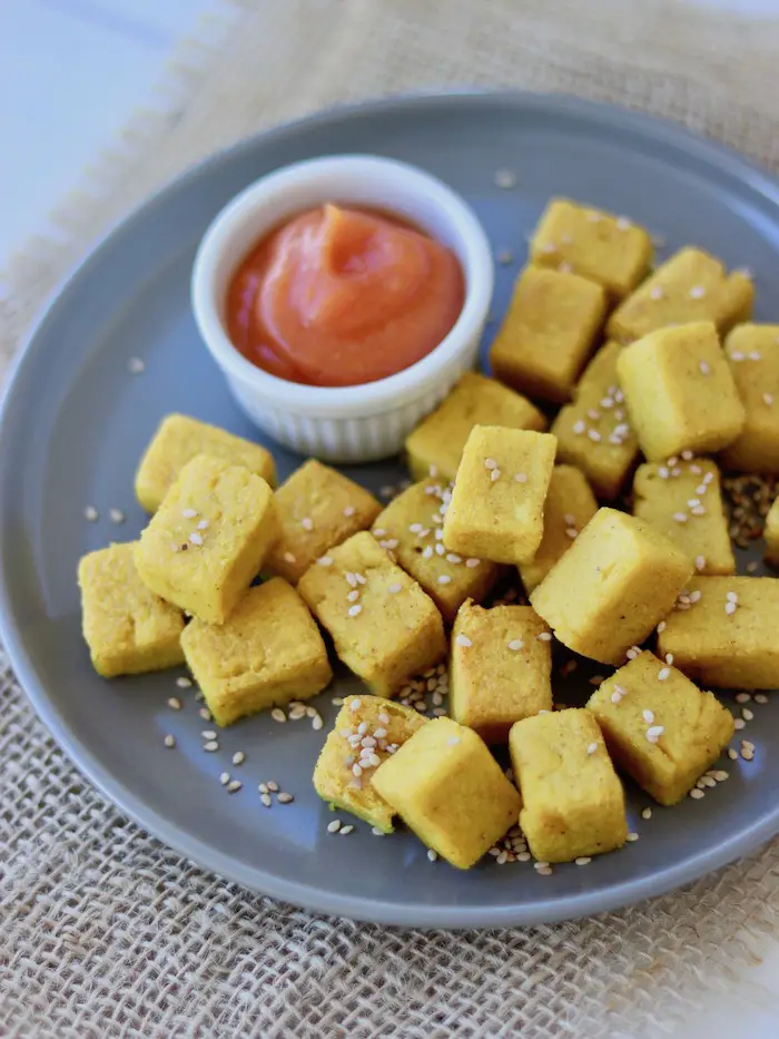 tofu de grão de bico (tofu birmanês) cortado em cubinhos e servido em um prato com ketchup caseiro