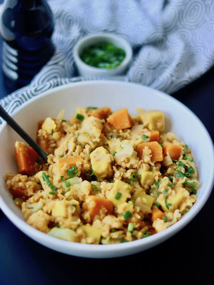 curry vegano de lentilha vermelha e tofu de grão de bico servido em um prato fundo com cebolinha fresca