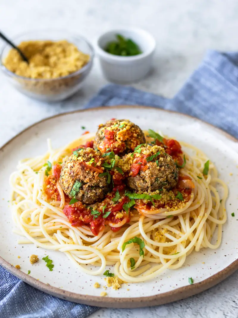 almôndegas de lentilha veganas servidas com macarrão espaguete, molho vermelho e parmesão vegano