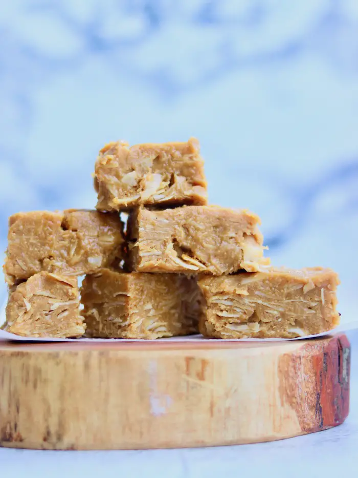 fudge vegano de amendoim e coco cortado em pedaços retangulares e empilhados em uma tábua de madeira