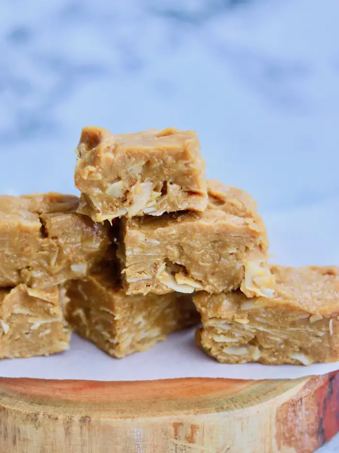 fudge vegano de amendoim e coco cortado em pedaços retangulares e empilhados em uma tábua de madeira