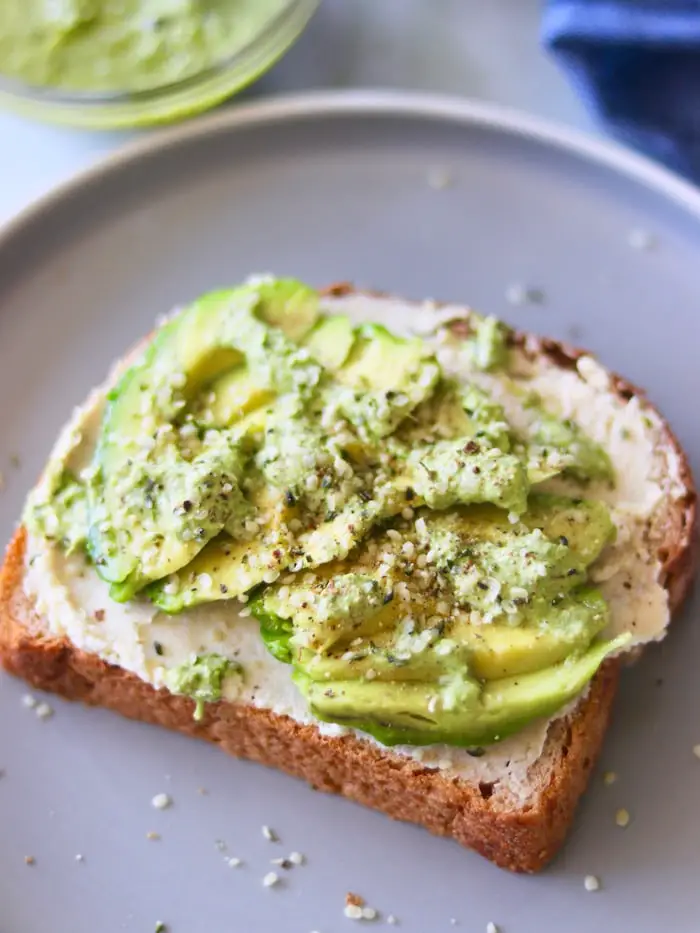 pão tostado servido com homus de grão de bico tradicional cremoso, avocado, sementes e molho de tahine com ervas frescas e limão