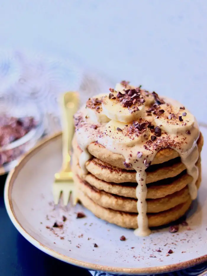 panqueca vegana de aveia e banana servida com creme de pasta de amendoim, banana e nibs de cacau