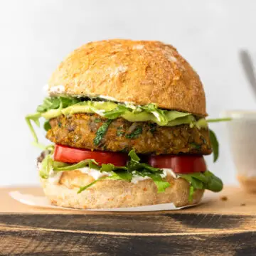 hambúrguer de lentilha servido com pão, maionese verde, tomate fresco e folhas verdes