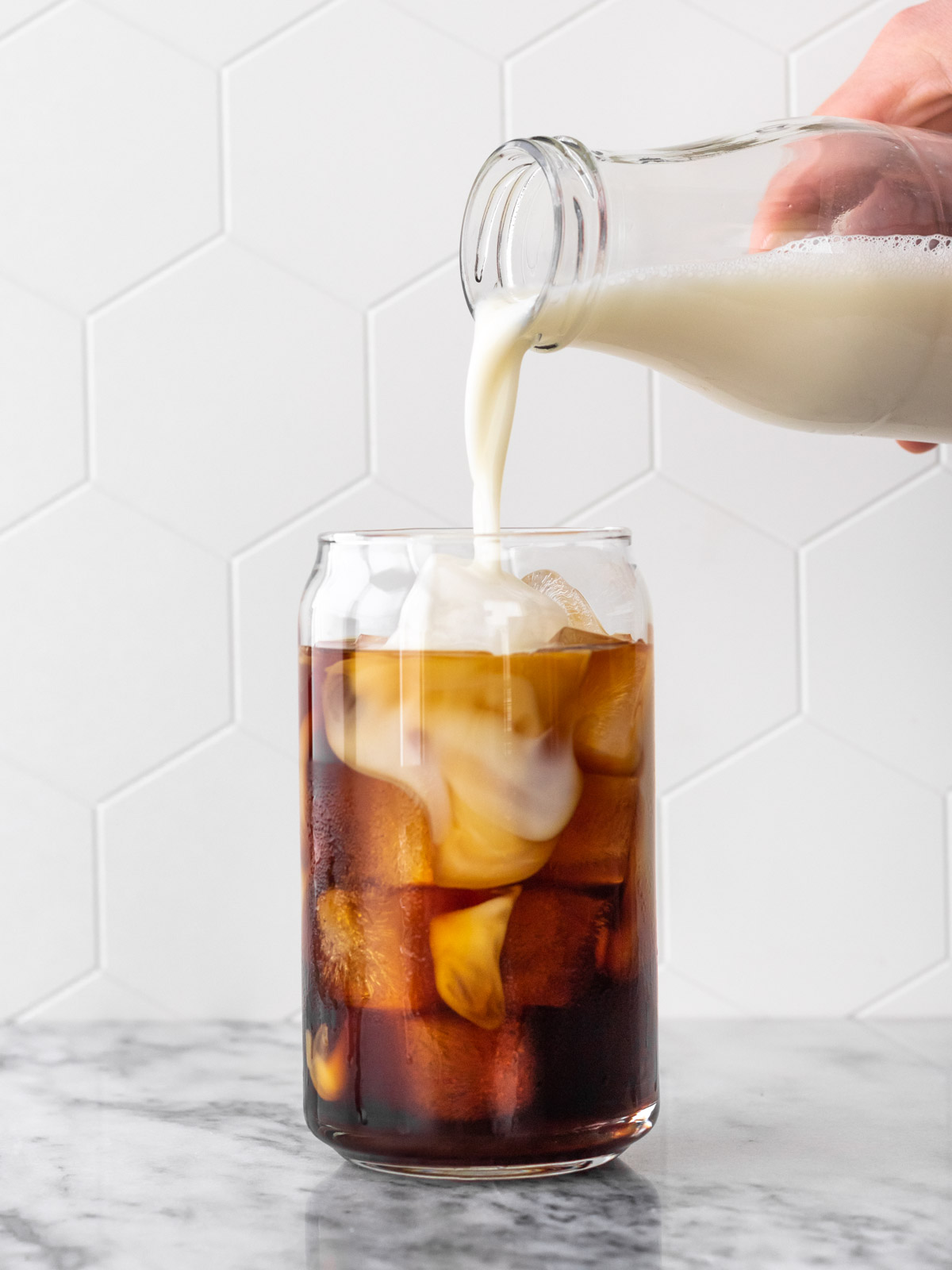 leite vegetal sendo adicionado em copo com café cold brew e cubos de gelo