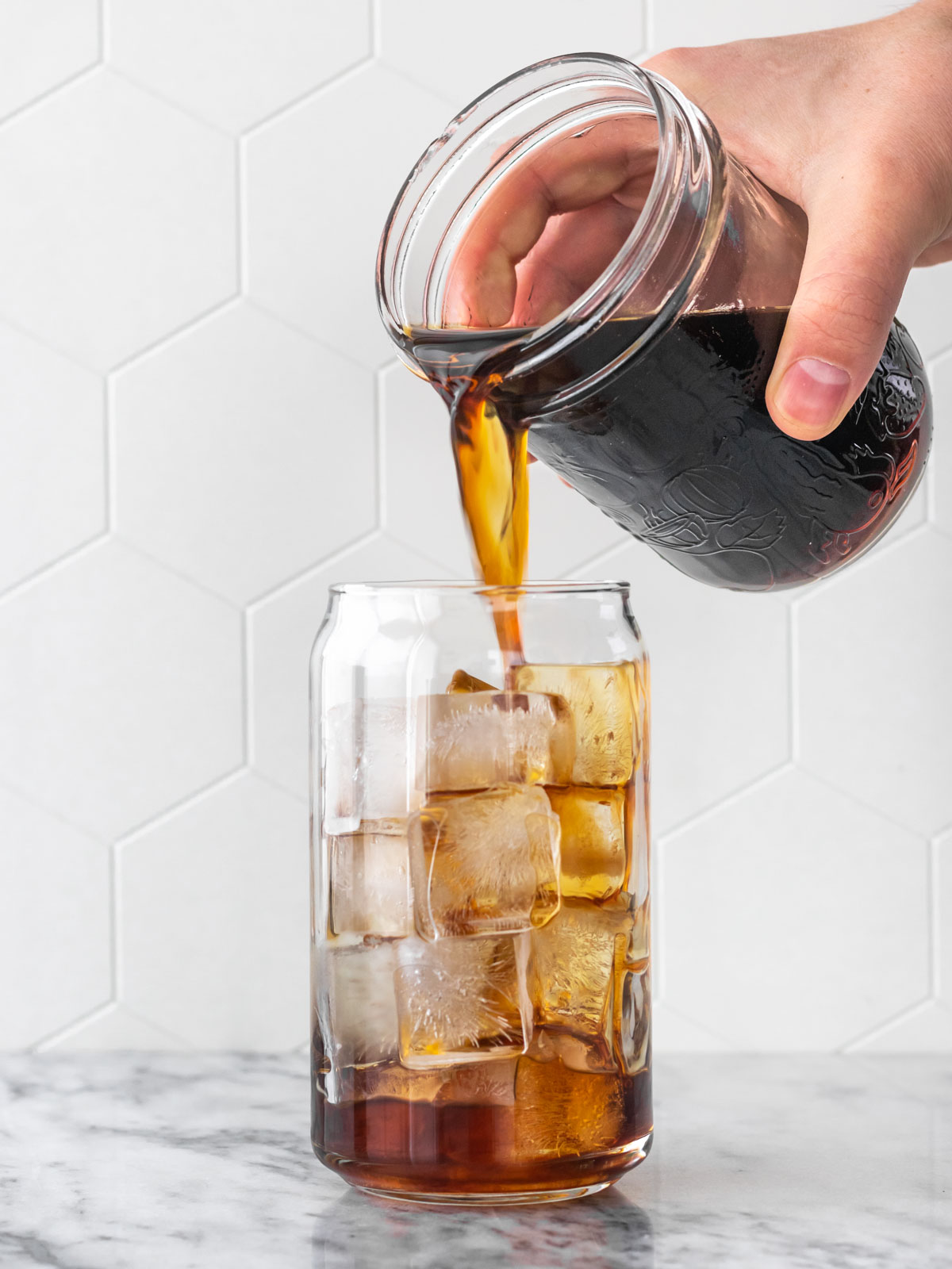 café cold brew sendo adicionado em um copo de vidro cheio de gelo em cubos