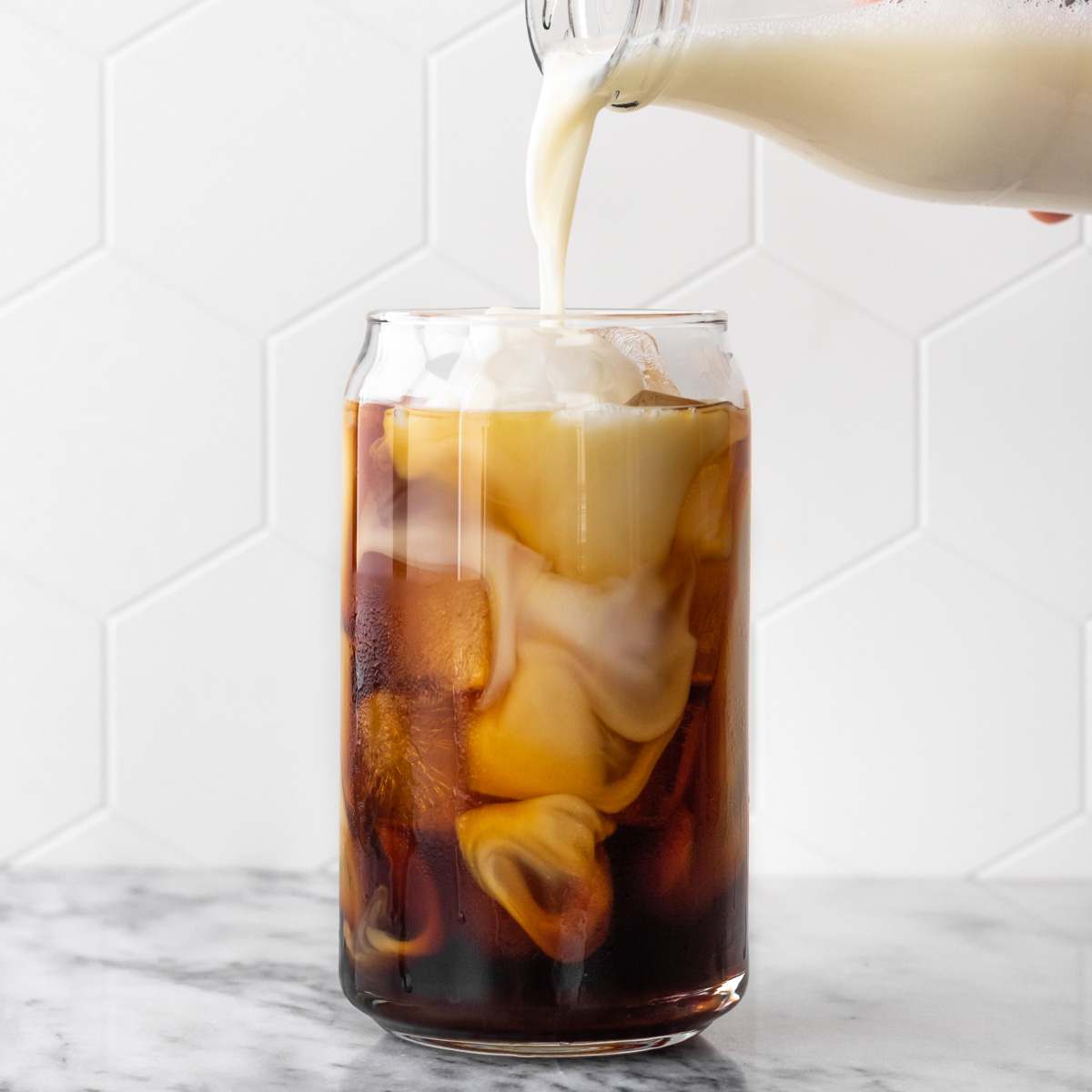 leite vegetal sendo adicionado em copo com café cold brew e cubos de gelo
