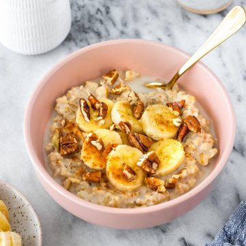 mingau de aveia servido em uma tigela com rodelas de banana, pitada de canela em pó e nozes-pecã picadas