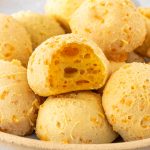 vista lateral de um prato com pães de queijo vegano, sendo que um deles está mordido, mostrando seu interior