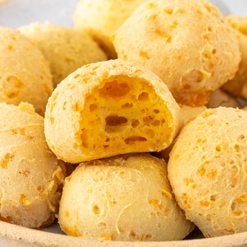 vista lateral de um prato com pães de queijo vegano, sendo que um deles está mordido, mostrando seu interior