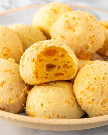 vista lateral de um prato com pães de queijo vegano, sendo que um deles está mordido, mostrando seu interior