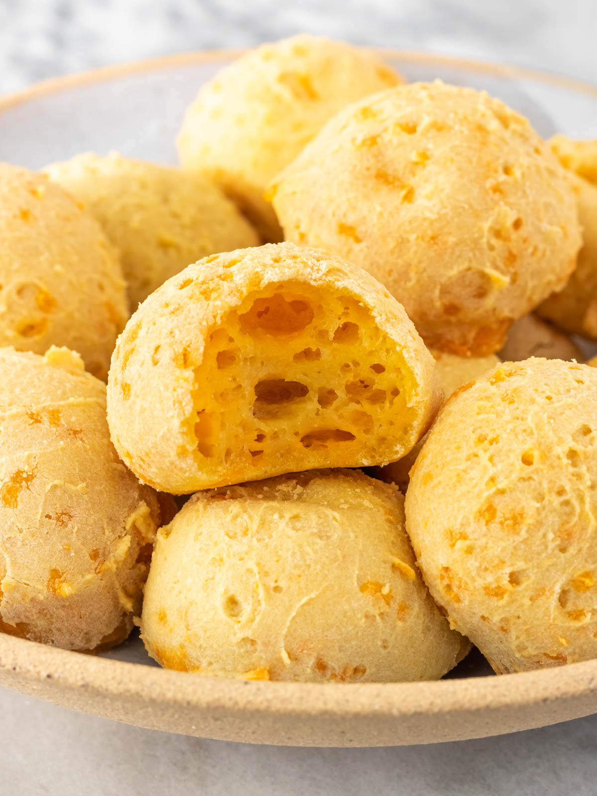 vista lateral de um prato com pães de queijo vegano, sendo que um deles está mordido, mostrando seu interior