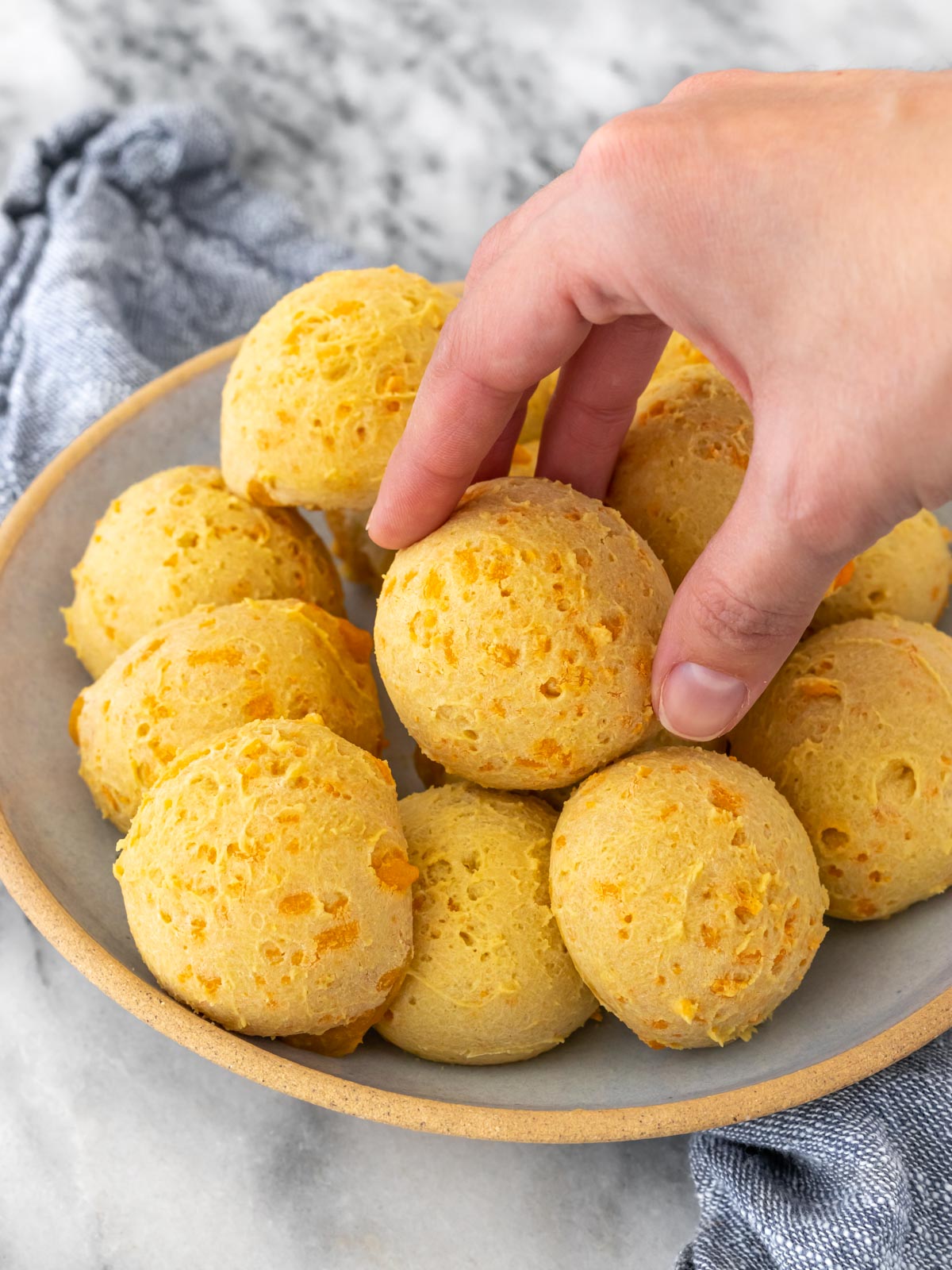 mão pegando um pão de queijo de um prato