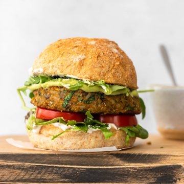 hambúrguer de lentilha servido com pão, maionese verde, tomate fresco e folhas verdes