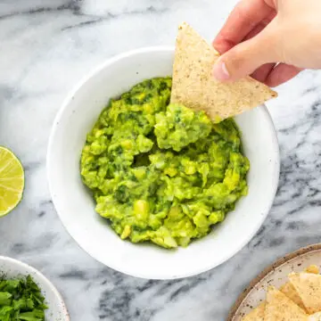 tortilla sendo inserida em um bowl de guacamole