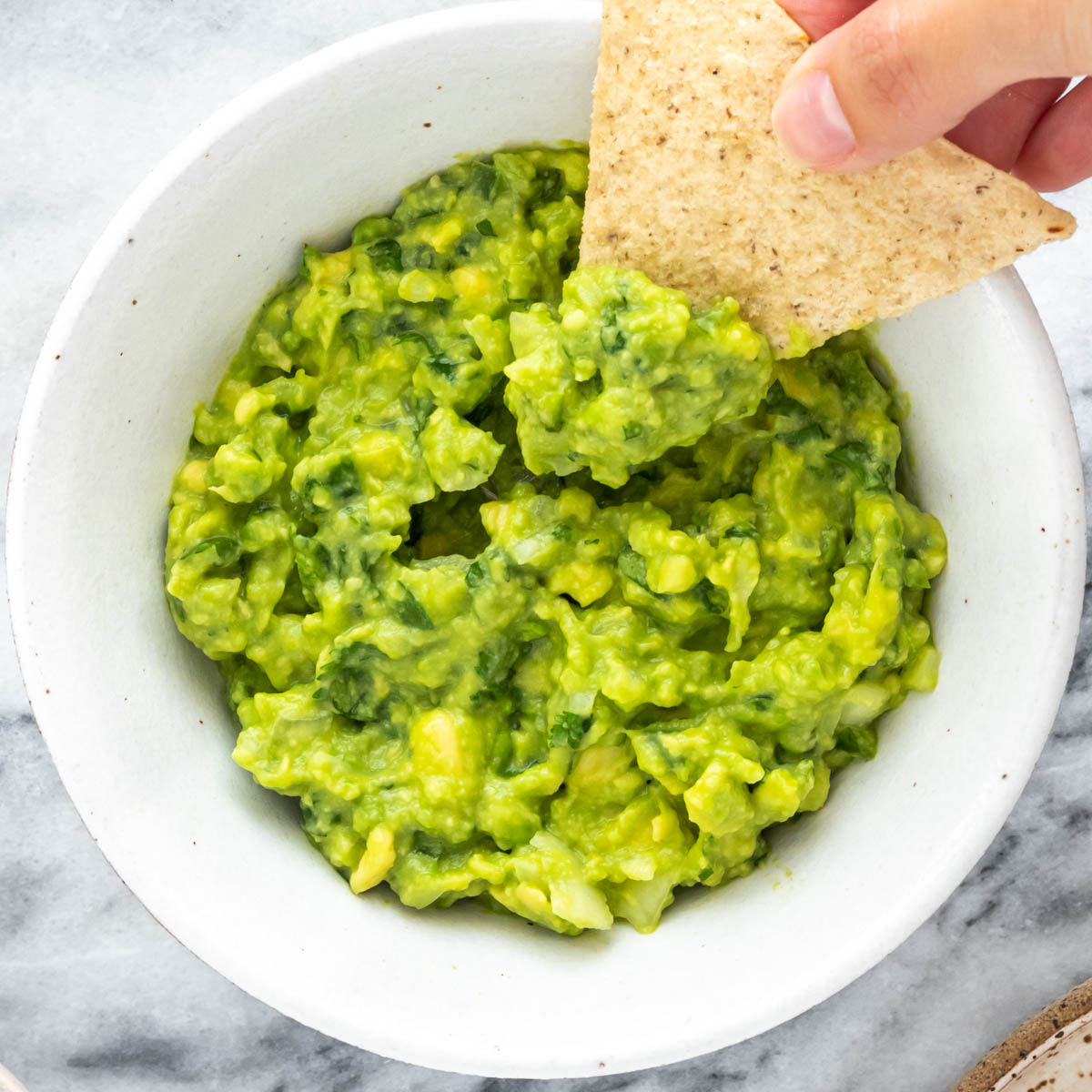 tortilla sendo inserida em um bowl de guacamole