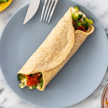 panqueca de aveia recheada com homus, brócolis, ervilha e tomate, servida em um prato azul