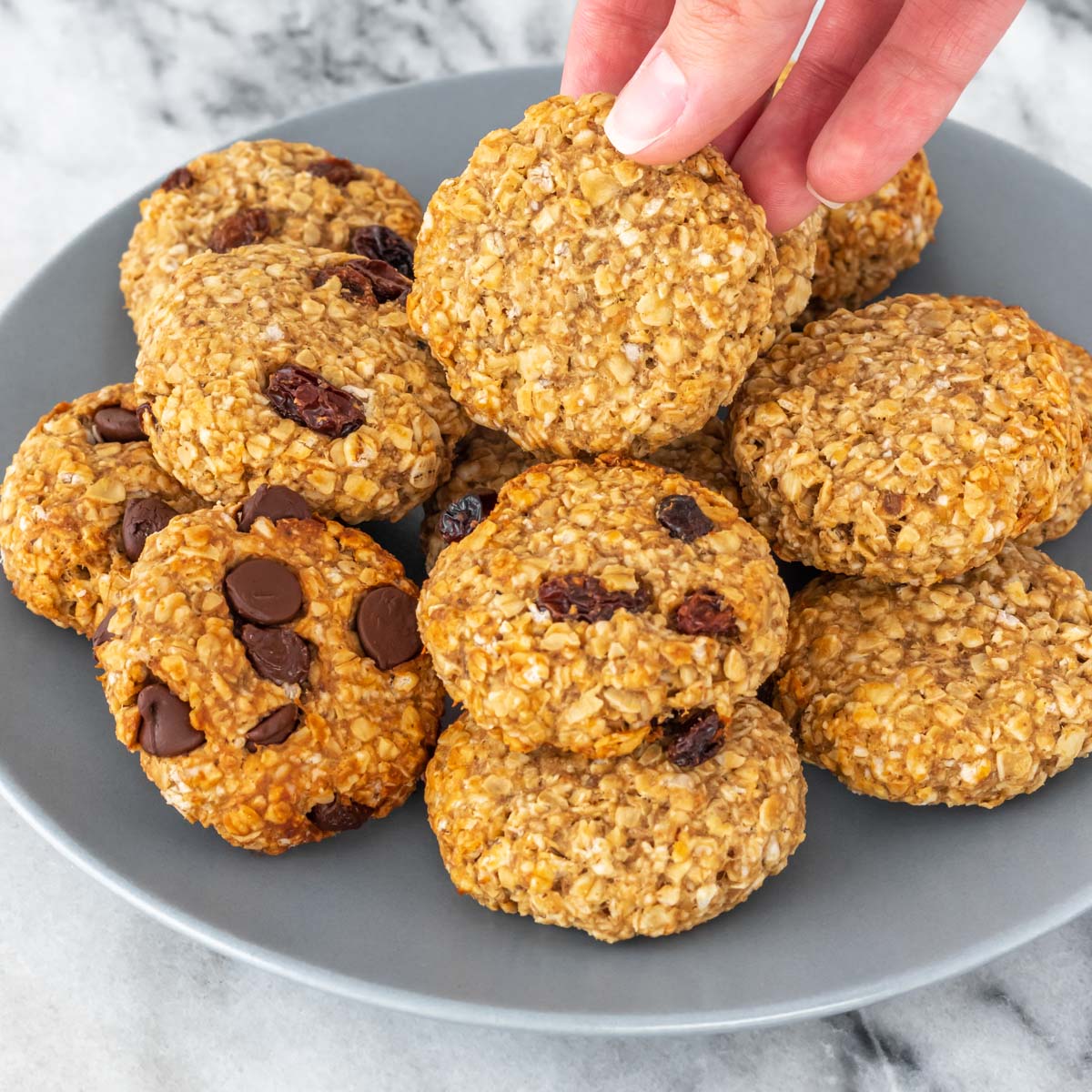cookie de aveia sendo retirado, com a mão, de um prato com outros cookies