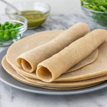 Duas panquecas de quinoa enroladas em cima de outras quatro panquecas empilhadas em um prato.