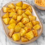 Batata assada na air fryer servida em um prato oval, acompanhada de maionese temperada com chipotle.