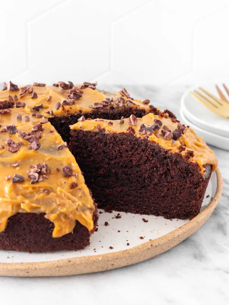 Bolo de chocolate, com cobertura de amendoim e nibs de cacau, cortado em uma fatia.