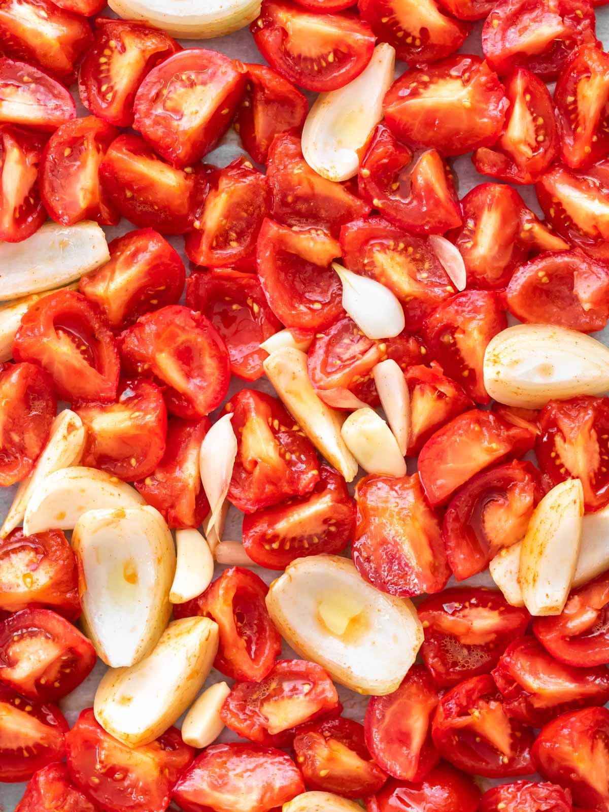 ingredientes para fazer molho de tomate caseiro, incluindo tomates, cebola, alho e temperos, distribuídos em uma assadeira, ainda crus