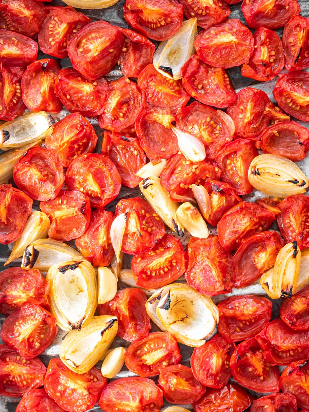 ingredientes para fazer molho de tomate caseiro, incluindo tomates, cebola, alho e temperos, distribuídos em uma assadeira e recém assados