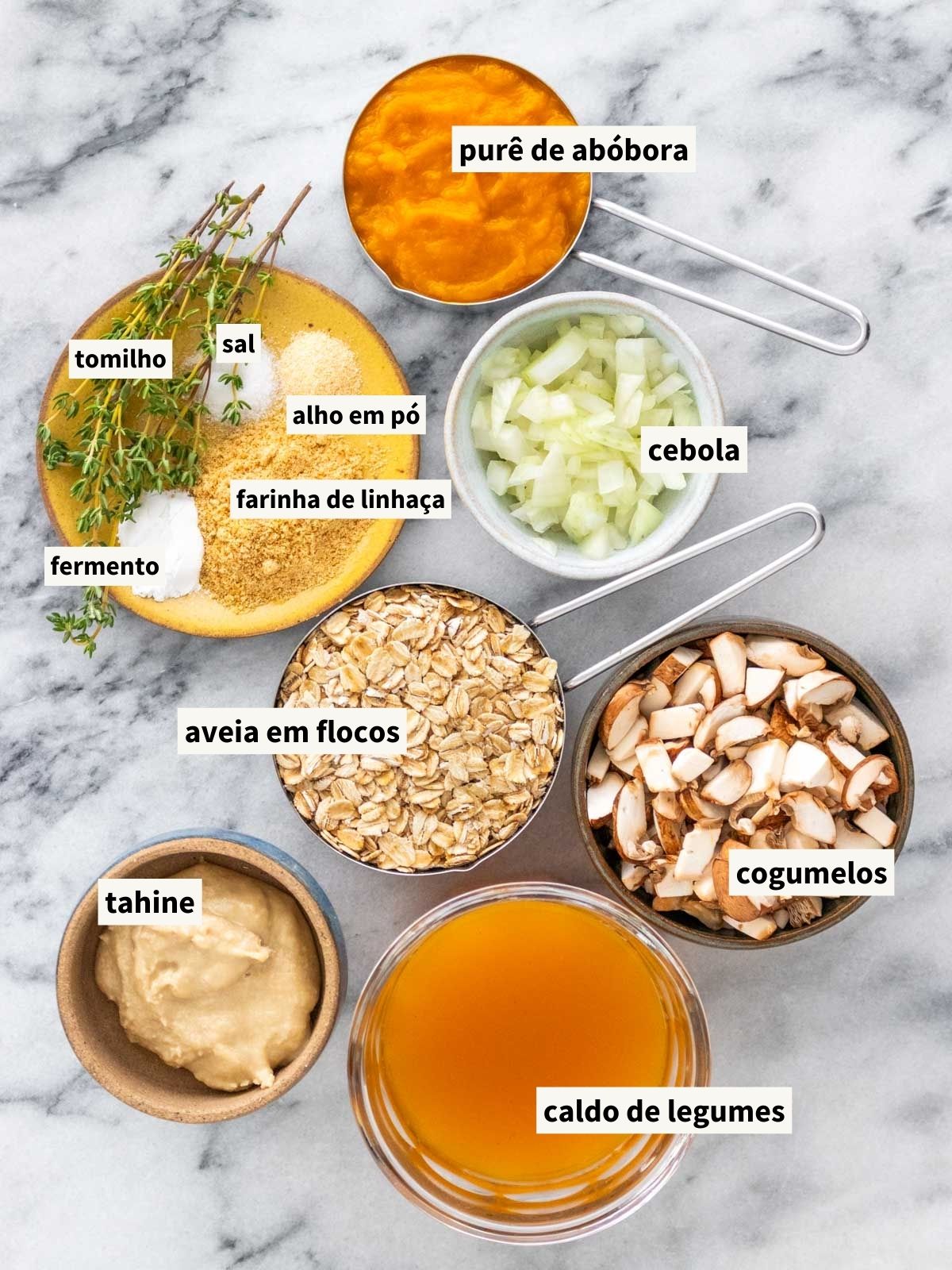 ingredientes para fazer muffins de aveia com abóbora e cogumelo, incluindo aveia em flocos grossos, purê de abóbora, cogumelos picados, tahine, caldo de legumes, cebola picada, sal, alho em pó, farinha de linhaça, fermento químico em pó e tomilho fresco