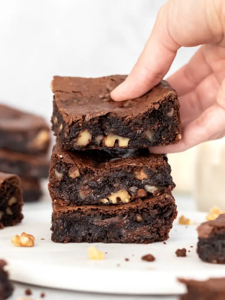 3 fatias de brownie de feijão empilhadas, mostrando seu interior dentro e molhado, com pedaços de nozes picadas e chocolate derretido