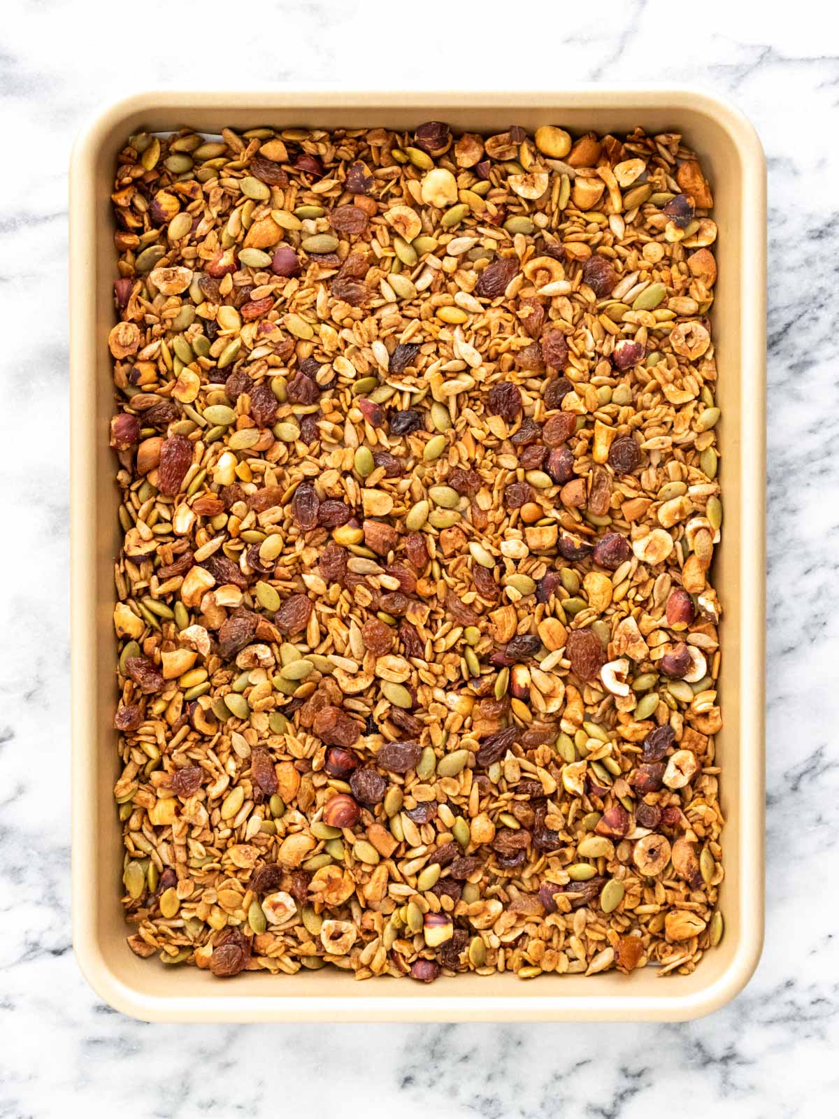 granola assada espalhada em uma assadeira e misturada com uvas-passas