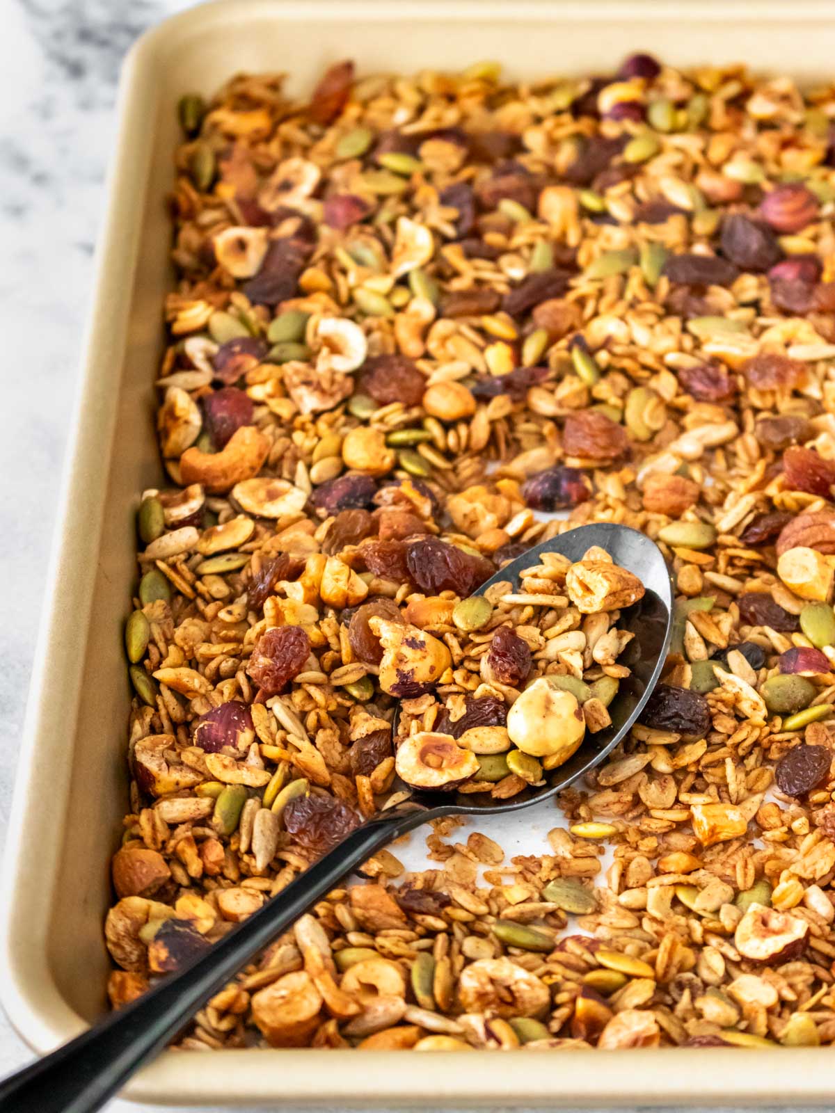 colher com granola caseira em uma assadeira com mais granola pronta