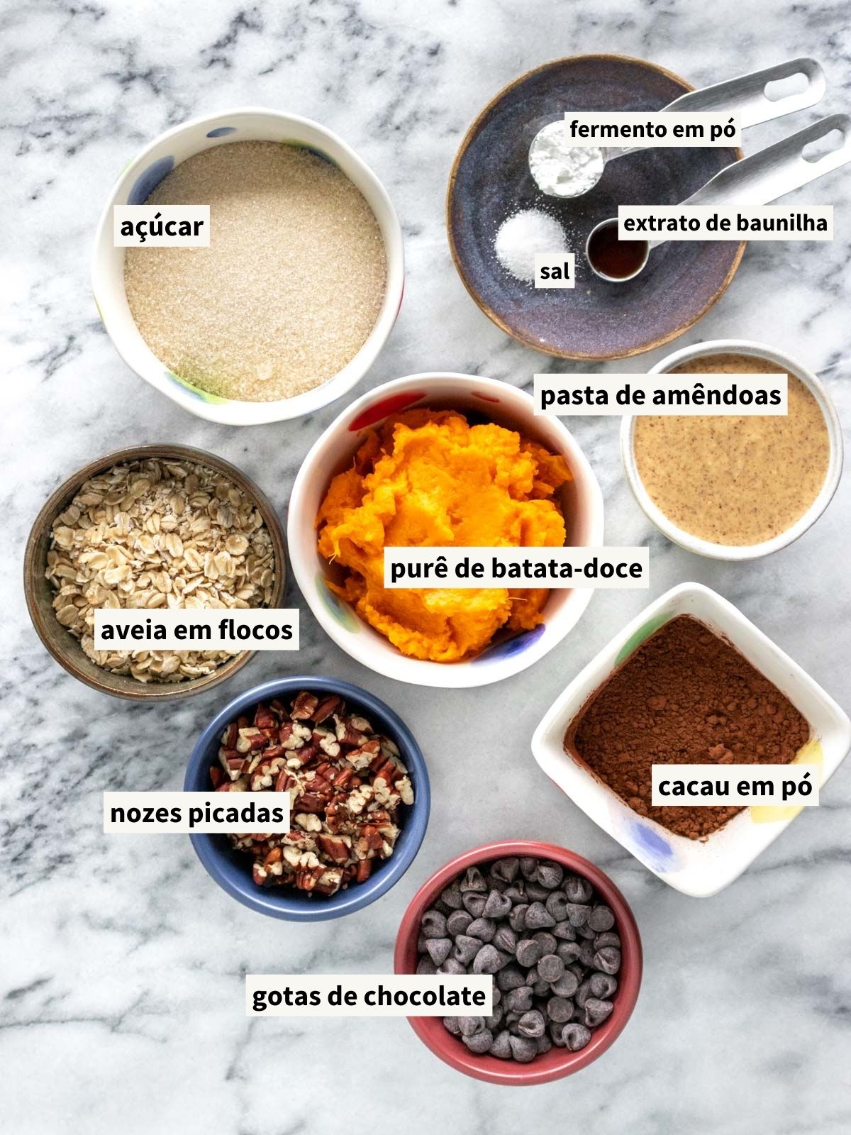 ingredientes para fazer brownie de batata-doce, incluindo aveia em flocos grossos, cacau em pó, açúcar cristal, sal, batata-doce assada, pasta de amêndoas natural, extrato de baunilha, fermento em pó, nozes picadas (nozes-pecã) e gotas de chocolate