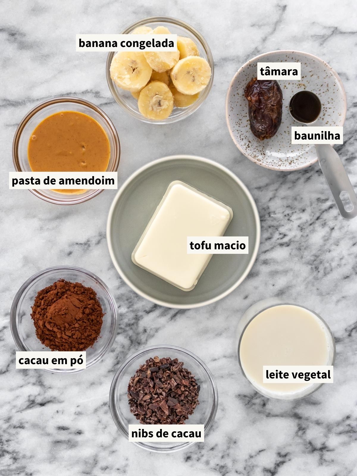 ingredientes para fazer smoothie de chocolate, incluindo tofu macio, banana congelada em rodelas, pasta de amendoim natural, cacau em pó, nibs de cacau, extrato de baunilha, tâmara medjool (jumbo) e leite vegetal.