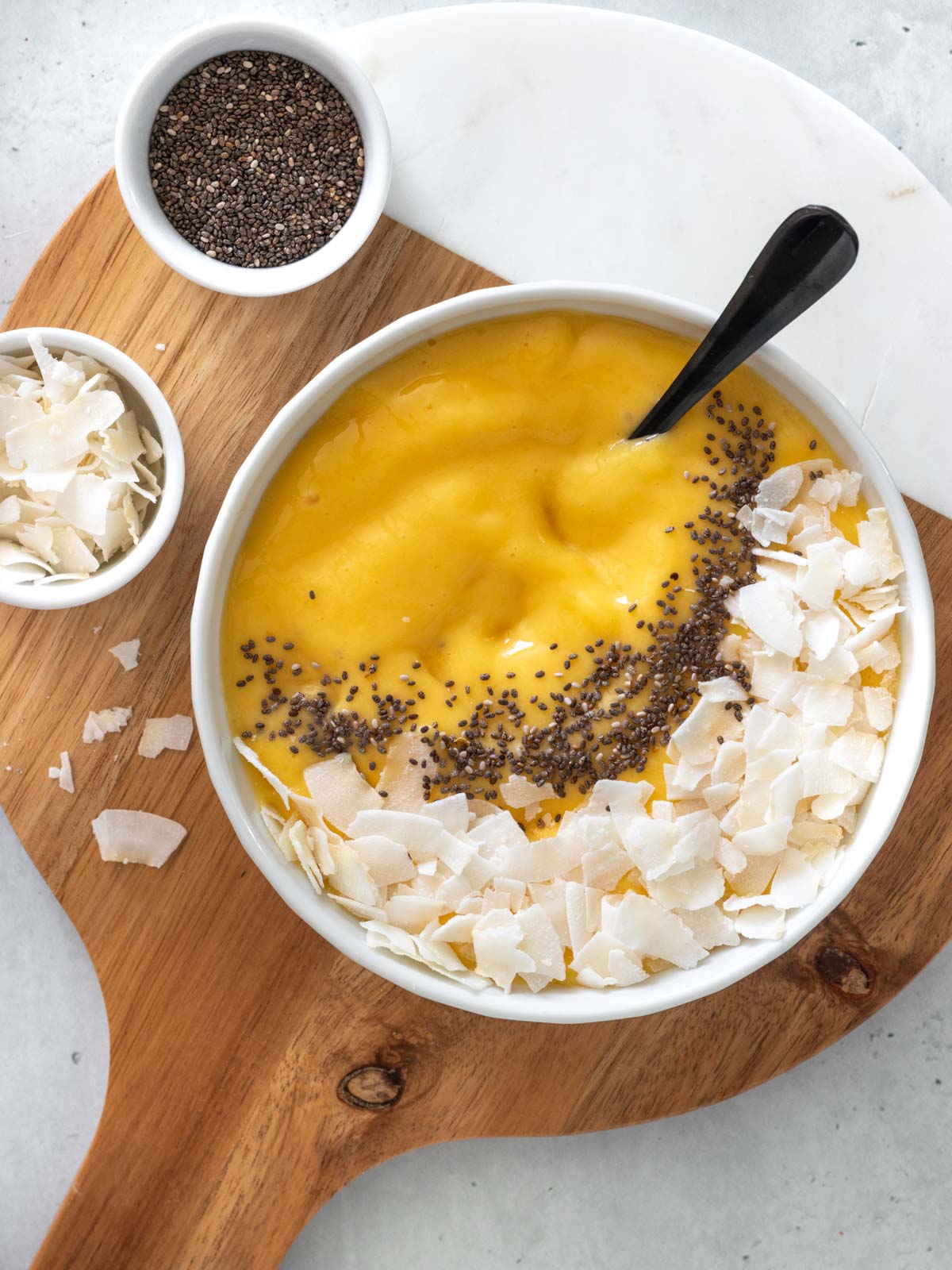 vitamina de manga com leite de coco servida na tigela com coco em fitas e sementes de chia