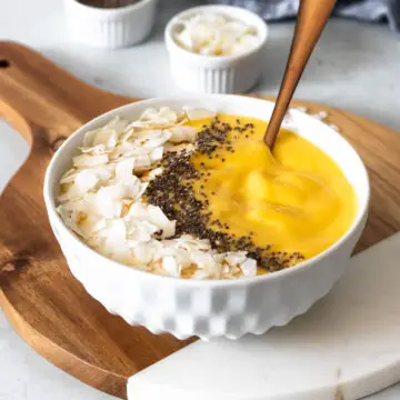 vitamina de manga feita com leite de coco servida na tigela com coco em fitas e sementes de chia