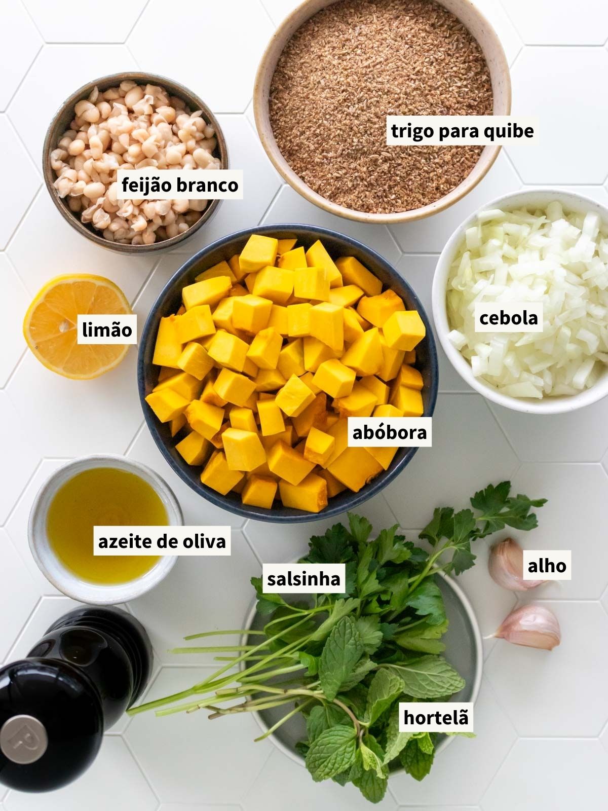 ingredientes para fazer quibe de abóbora na travessa, incluindo trigo para quibe (triguilho, trigo bulgur), hortelã fresca, azeite de oliva, cebola, sal, alho, abóbora cabotiá, salsinha fresca, pimenta-do-reino, feijão-branco cozido e limão siciliano