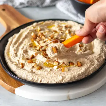 palito de cenoura sendo inserido em prato com patê de amêndoas vegano feito com resíduo de leite vegetal, mostrando sua textura cremosa