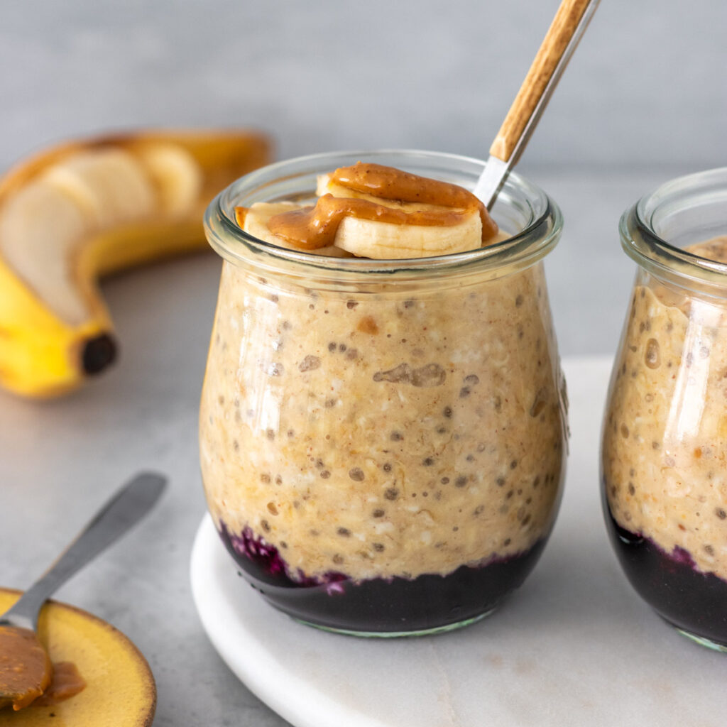 overnight oats de banana com pasta de amendoim servido em um potinho pequeno com geleia no fundo e rodelas de banana e mais pasta de amendoim por cima