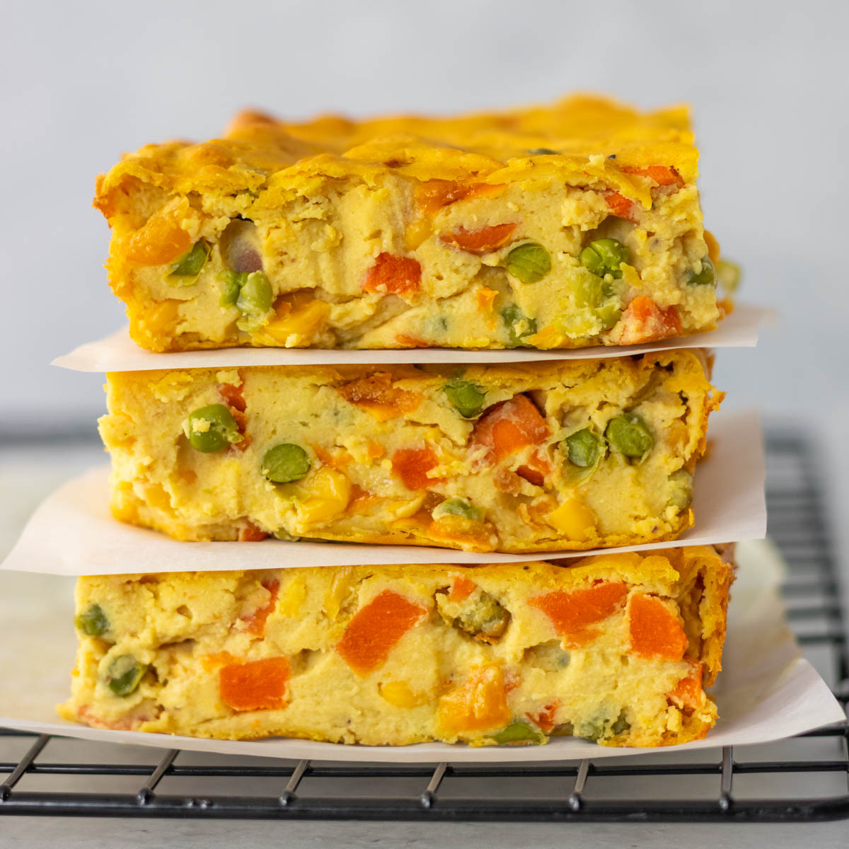 três pedaços de torta de legumes vegana empilhados e separados por um pedaço de papel antiaderente