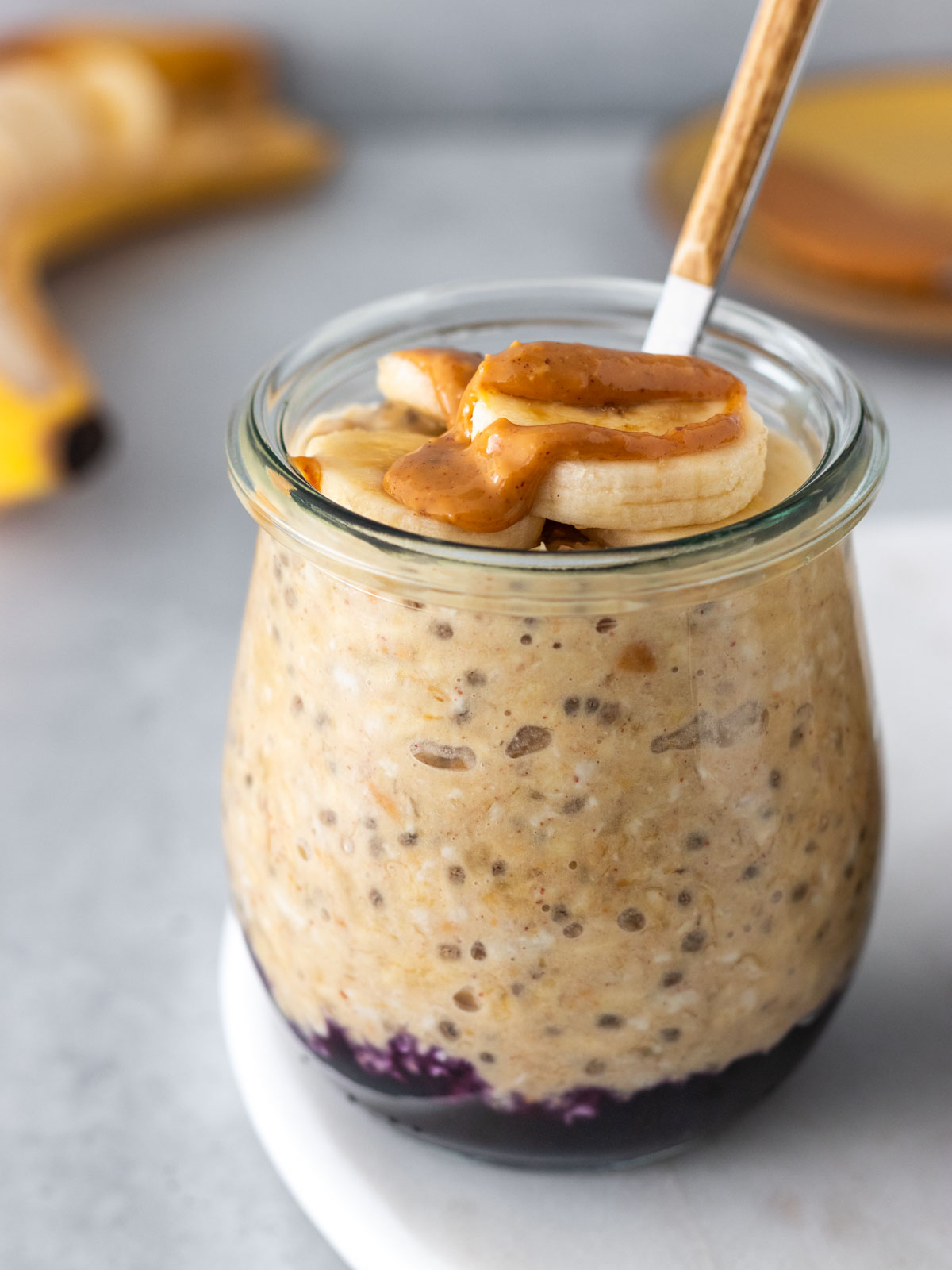 overnight oats de banana com pasta de amendoim servido em um potinho pequeno com geleia no fundo e rodelas de banana e mais pasta de amendoim por cima