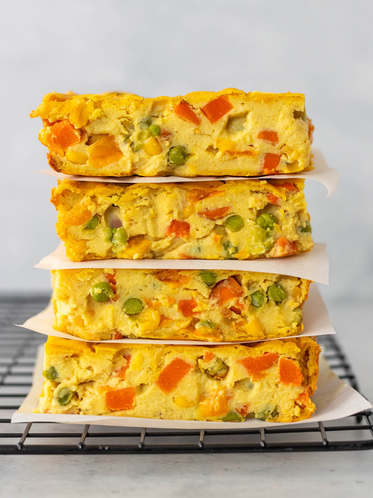 quatro pedaços de torta de legumes vegana empilhados e separados por um pedaço de papel antiaderente