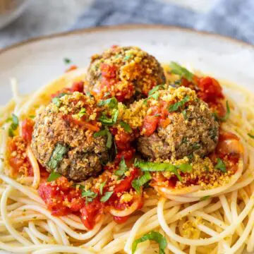 almôndegas de lentilha servidas com macarrão e molho vermelho e polvilhadas com parmesão vegano e ervas frescas