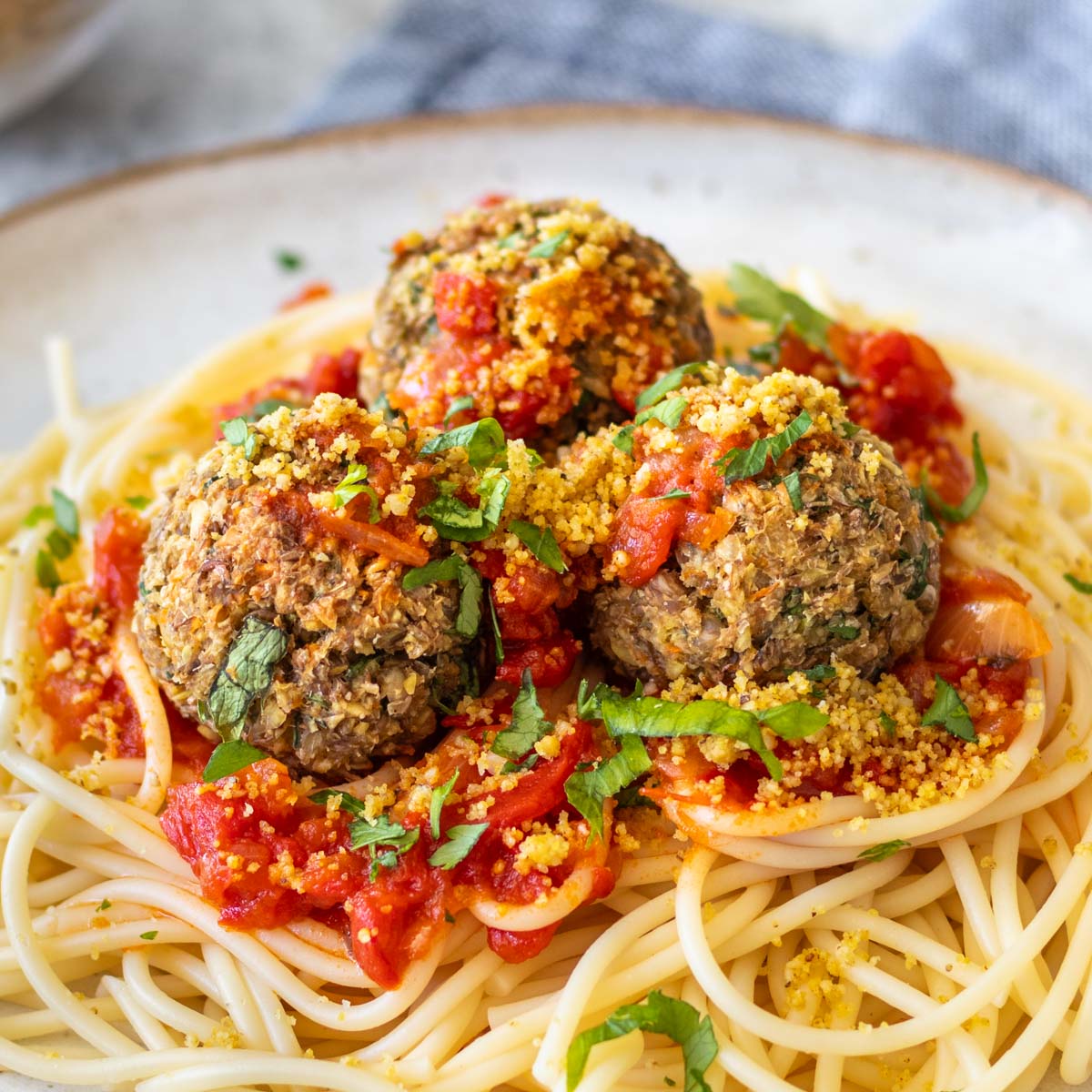 almôndegas de lentilha servidas com macarrão e molho vermelho e polvilhadas com parmesão vegano e ervas frescas