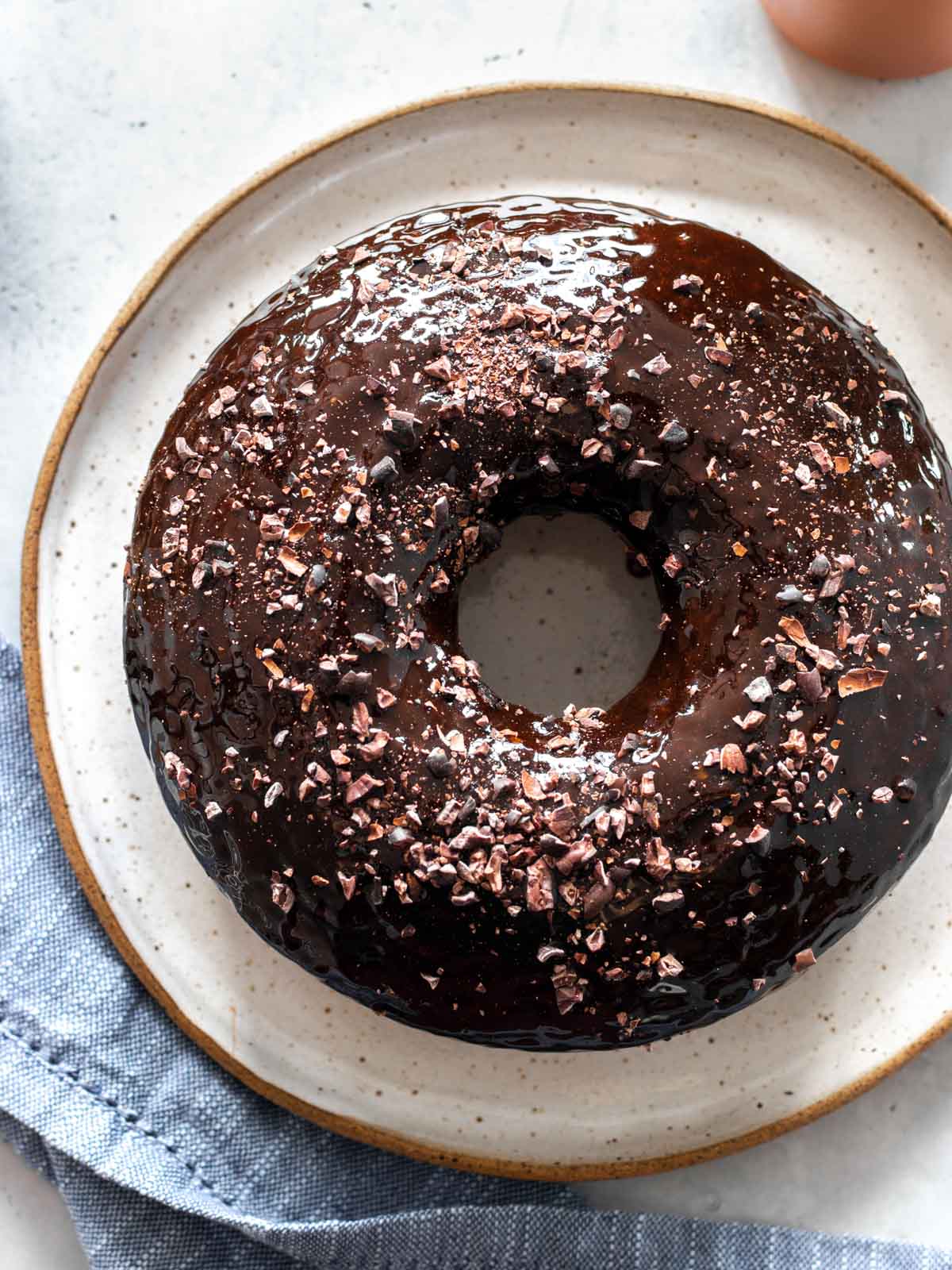 bolo de chocolate vegano servido em prato com cobertura de calda de chocolate e nibs de cacau